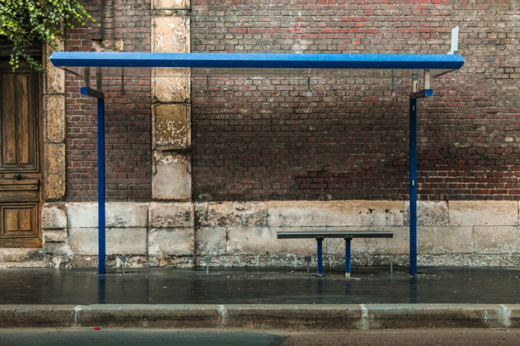 An empty bus stop with a bench and shelter against a brick wall on a wet street.