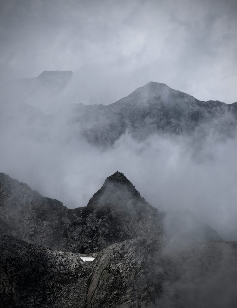 Rocky mountain peaks partially obscured by fog, with layered ridges visible through mist and soft gray sky above.